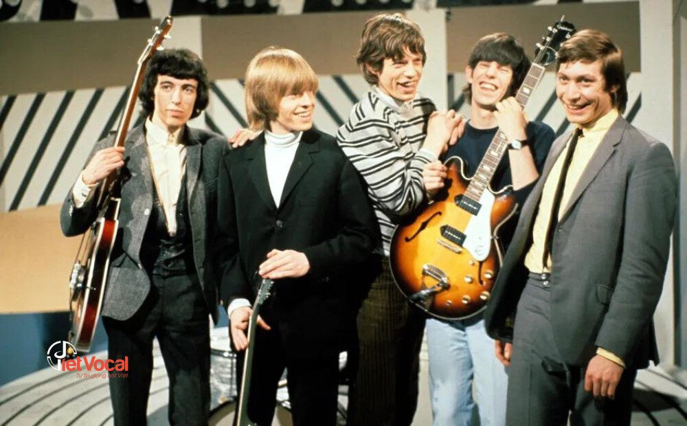 alt text: Ban nhạc The Rolling Stones biểu diễn trên sân khấu, với Mick Jagger hát chính, Keith Richards chơi guitar, Ronnie Wood chơi guitar và Charlie Watts chơi trống.